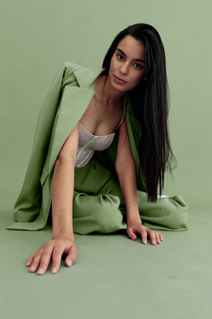 Young woman wearing a pastel green suit and lace top poses on a matching green floor and background, showcasing modern fashion with a calm, poised expression.の写真素材