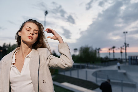 Young woman in beige coat enjoying evening outdoors with eyes closed, serene expression, soft natural light and urban background at sunset key fashion, woman, evening, serene, outdoor, coat, sunsetの写真素材