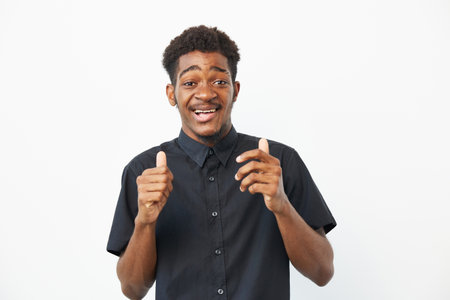 Happy African American man expressing excitement and joy with a cheerful smile against a clean white background, showcasing a casual outfit and positive energy.の写真素材