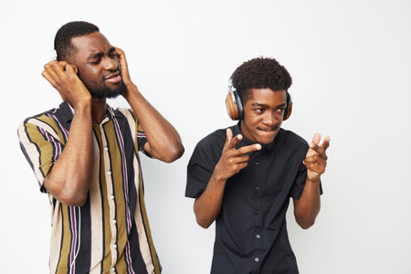 Two black men enjoying music together, one smiling while the other reacts dramatically. The joyful atmosphere captures friendship and fun moments.の写真素材