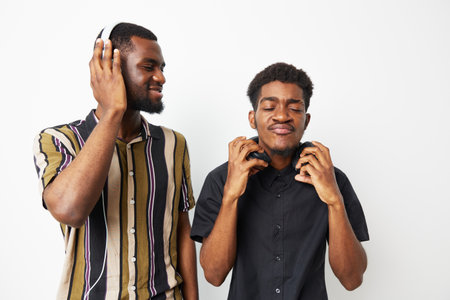 Two smiling African American men enjoying music together with headphones on. The scene radiates joy and connection, showcasing a fun moment of friendship.の写真素材