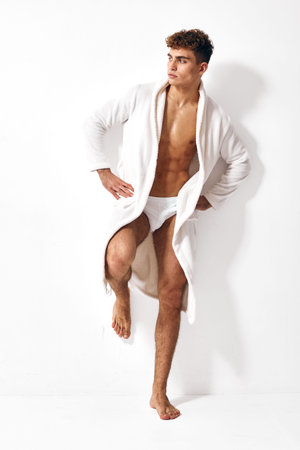 Stylish young man in white bathrobe posing confidently against a bright background. Fashion and self-care concept for modern lifestyles and beauty standards.の写真素材