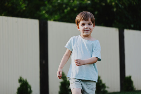 Cheerful boy running in the garden, wearing casual light blue clothes with a happy expression,...