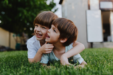 Playful children enjoying a sunny day, smiling joyfully while lying on the green grass, embracing each other with happiness and carefree spirit. ###の写真素材
