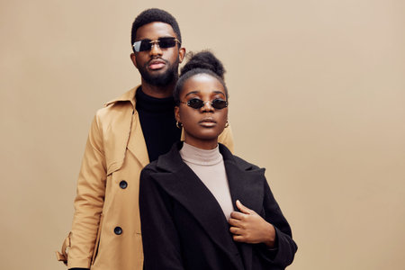 Stylish couple wearing sunglasses, posing confidently against a warm beige background, showcasing modern fashion and urban elegance in a seasonal autumn settingの写真素材