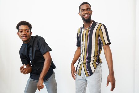 Two smiling Black men express joy and camaraderie, showcasing vibrant fashion and modern style in a bright, minimalist environment. A true celebration of friendship.の写真素材