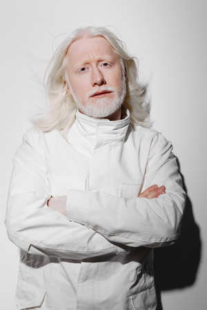 Portrait of a senior man with long white hair and beard, wearing a white outfit, standing...