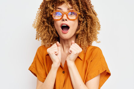 Excited woman with curly hair and glasses expressing joy against a plain background Bright orange...