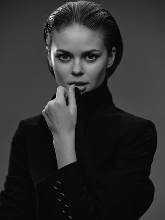 black and white portrait of a confident woman with slicked-back hair and a thoughtful expression wearing a dark turtleneck against a plain dark backgroundの写真素材