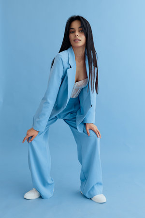 Young woman wearing a light blue suit poses confidently against a matching blue background, showcasing modern fashion and casual style with long straight hair.の写真素材