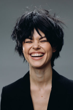 smiling woman with short black hair laughing joyfully wearing a black blazer on gray background expressing happiness and energyの写真素材