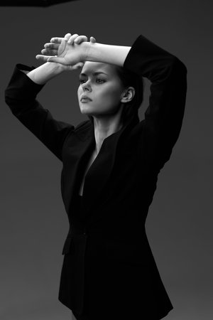 black and white woman posing with raised arms wearing dark blazer against dark background in dramatic studio lightingの写真素材
