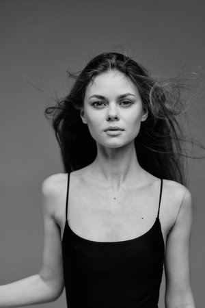 Black and white portrait of a young woman with long hair wearing a black spaghetti strap top,...