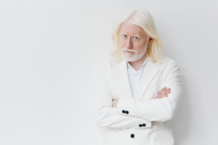 Portrait of a confident older man with long white hair wearing a stylish white suit, arms crossed, against a clean, minimalist light background, exuding wisdom and eleganceの写真素材