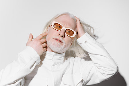 Fashion portrait of a modern man with white hair and beard, wearing stylish glasses, posing against a minimalistic white background Unique and artistic style with a touch of sophisticationの写真素材