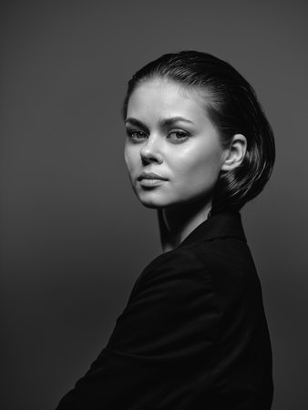black and white portrait of a woman with short hair wearing a dark jacket looking serious on gray...