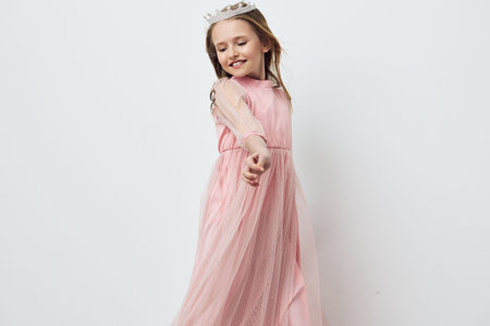 Young girl in a pink dress posing happily, showcasing elegance and joy against a soft white background Perfect for children s fashion and celebration themesの写真素材