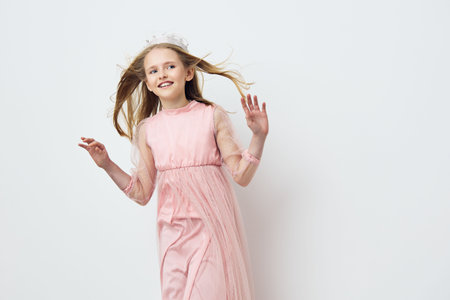 Young girl in a pink dress joyfully dancing against a minimalistic light background, capturing the essence of childhood happiness and innocenceの写真素材