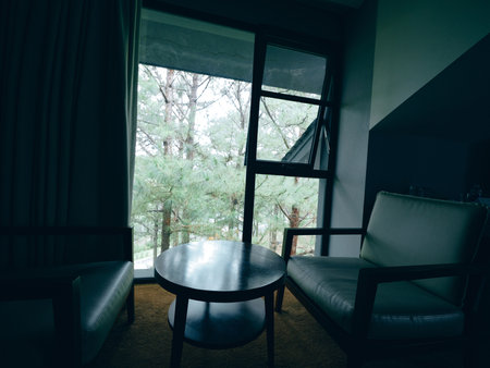 Cozy seating area with two armchairs and a round table, framed by a large window overlooking green...