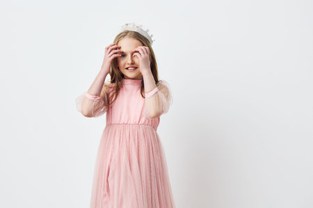 A joyful young girl wearing a pink dress with sheer sleeves and a floral crown, expressing happiness...