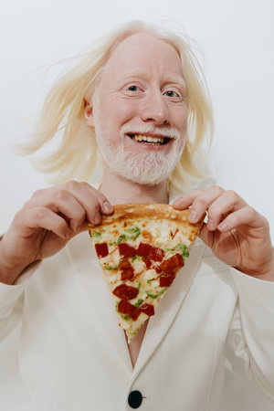 Man with long white hair holding a slice of pizza, dressed in a white suit against a plain white background, showcasing happiness and enjoyment of food with vibrant colorsの写真素材