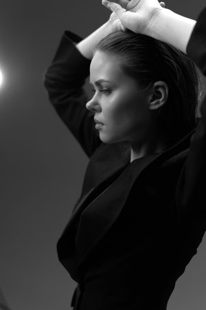 Black and white portrait of a serious woman in a dark jacket with hands raised, showing strong emotion and elegant style.の写真素材