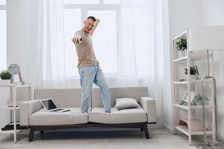 Energetic man dancing on couch, embracing digital detox while enjoying a creative moment. A vibrant expression of joy amidst the chaos of modern life.の写真素材