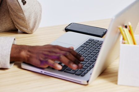Close-up of a person working on a laptop with a smartphone and stationery on a wooden desk, representing modern office environment and remote work, lifestyle concept.の写真素材