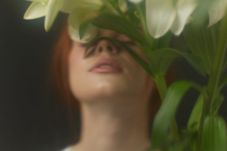 Young woman with red hair interacting with white lilies, showcasing tranquility and elegance in a soft focused composition, ideal for wellness and floral aestheticsの写真素材