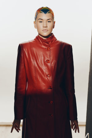 Woman with colorful short hair wearing a red leather coat, standing confidently against a soft, light background in a modern fashion portrait.の写真素材