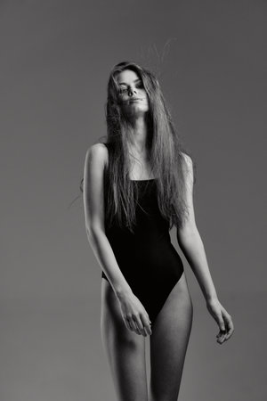 Black and white portrait of a tall woman with long hair wearing a black bodysuit posing against gray background.の写真素材