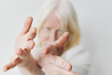 White haired person reaching out with hands against a plain background, conveying a sense of longing...