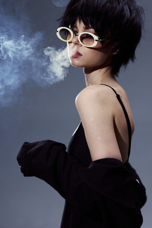 Stylish woman wearing sunglasses exhaling smoke with a confident expression in a dark moody setting