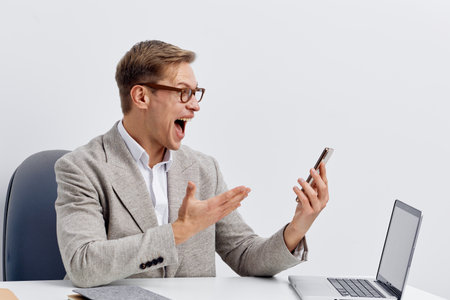 excited man chatting with AI on smartphone at desk laptop casual suit glasses digital communication...