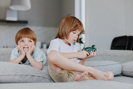 Two young boys engaging in play, one focused on a toy car while the other looks intrigued, creating...
