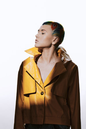 woman with colorful shaved hair wearing a yellow leather jacket poses with confidence against a white background in studio lightingの写真素材