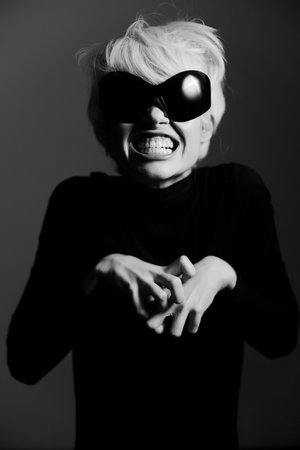 Playful person with short blonde hair wearing oversized black sunglasses, making a funny face...