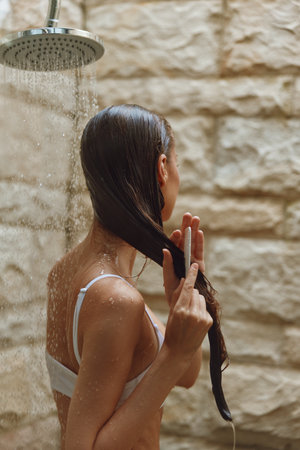Woman washing hair under outdoor shower with wet skin and long dark hair, natural light, rustic...