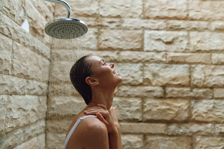smiling woman enjoying outdoor shower with stone wall background, fresh water drops, relaxed mood,...