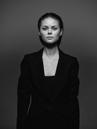Black and white portrait of a serious woman in a dark jacket with neutral expression and clean...