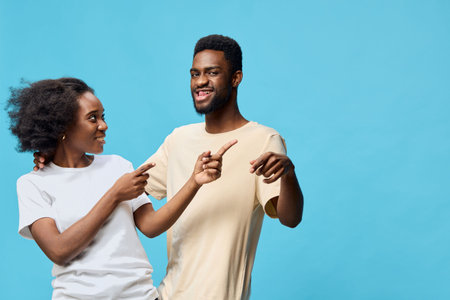 Young couple smiling and pointing at each other against a bright blue background, showcasing joy and connection in a playful momentの写真素材