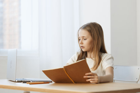 Young girl studying at a desk with a laptop, focused and thoughtful, surrounded by bright natural...