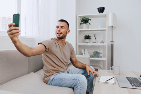 Happy man taking a selfie in a cozy, modern living room, surrounded by stylish decor and natural...