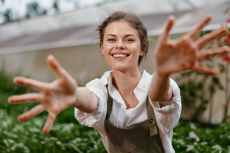 Smiling young woman in a garden, wearing an apron and reaching out, expressing joy in a vibrant green setting for healthy lifestyle conceptsの写真素材