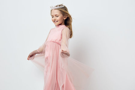 A joyful young girl in a flowing pink dress twirls gracefully, showcasing her playful spirit and innocence in a minimalist studio setting with soft pastel tonesの写真素材