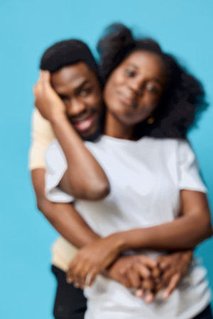 A joyful young African couple embracing in a playful moment against a vibrant blue background, showcasing love, happiness, and connectionの写真素材