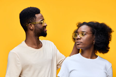Happy young couple wearing sunglasses, with a vibrant yellow background, showcasing love and connection through playful emotions and stylish fashionの写真素材