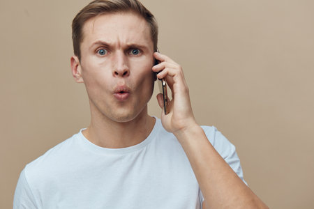 shocked young caucasian man talking phone facial expression casual wear isolated neutral background digital detox conceptの写真素材