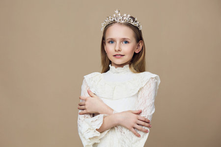 Young girl in a delicate white dress with a crown, exuding elegance and innocence, posed against a...