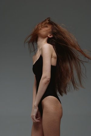 Woman with long hair in black outfit posing against grey background, elegant, dynamic, artistic,...